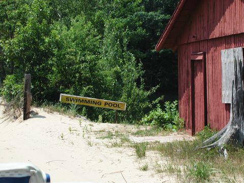 1992 Ford Taurus - A portion of a white vehicle is visible in the foreground, with a yellow 'SWIMMING POOL' sign and a red building in the background.