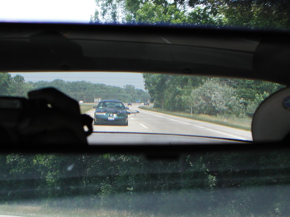 Car seen from inside another car, driving on a highway. Trees and sky visible