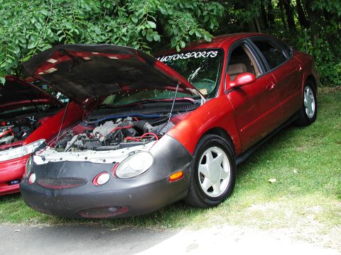 1992 Ford Taurus - A red sedan, possibly a 1996 Ford Taurus, is parked on grass with its hood open, revealing the engine compartment.