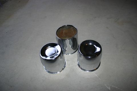 2003 Jeep TJ - Three chrome hubcaps are arranged on a gray concrete floor.