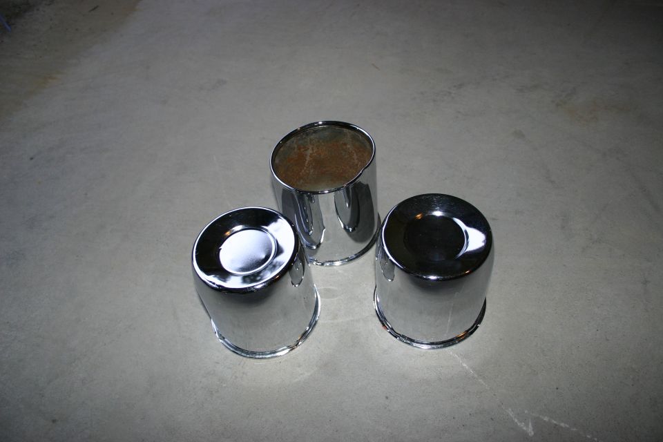 Three chrome hubcaps on a concrete surface