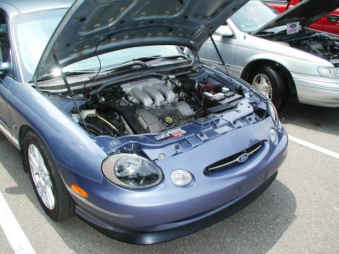1992 Ford Taurus - Front view of a blue car with its hood open, revealing the engine. Another car is visible in the background.