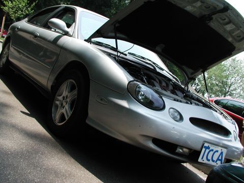 1992 Ford Taurus - Silver sedan with hood open, parked outdoors. A red car is partially visible in the background.