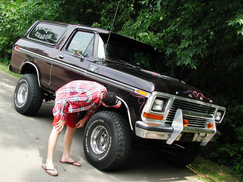 1978 Ford Bronco with custom pinstriping and a person checking the front tire. "Black Shadow" is on the rear window