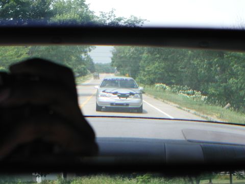 1992 Ford Taurus - A silver sedan is seen from behind on a rural road, with trees lining the sides.
