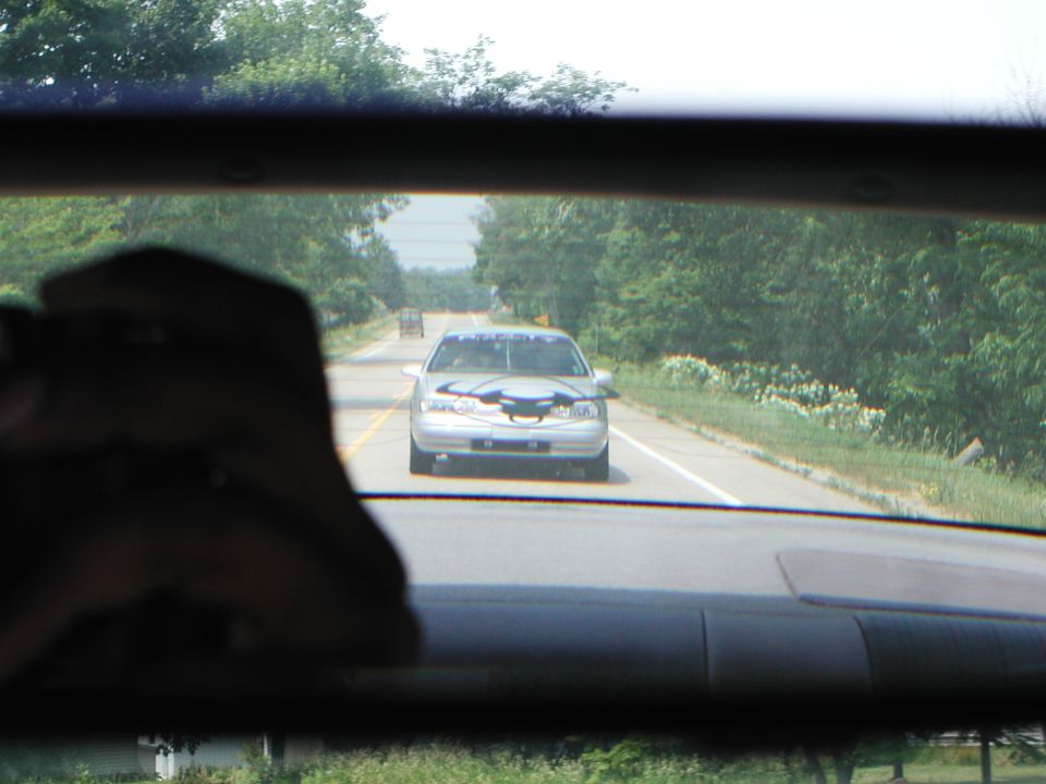 Silver sedan with a dark graphic on the hood, driving on a two-lane road