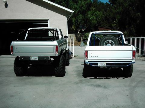 1978 Ford Bronco - Two Ford Broncos, a silver lifted model and a white one with a spare tire, are parked side-by-side in a driveway.