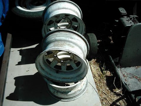 1978 Ford Bronco - A stack of four old, weathered rims sits on a concrete surface next to some debris.