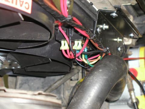 1988 Ford Bronco - Close-up of an electric fan controller module and relay wiring mounted on a black steel bracket, with heavy red power leads and green, yell…