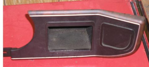 1988 Ford Bronco - Removed brown/burgundy plastic dash bezel panel lying face-up on a red workbench, with a rectangular open cubby pocket in the center and a…