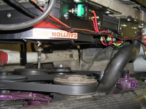 1988 Ford Bronco - Looking up from below at a finished electric fan install, with the fan's black shroud and its upside-down red-and-white CAUTION decal bolte…