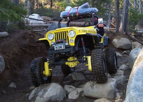1998 Ford Ranger - A yellow Jeep navigates a rocky trail, equipped with a winch and gear on its roof rack.