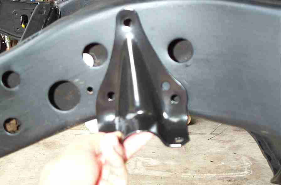 Hand holding a black steel bracket with holes in front of a black frame section with round holes