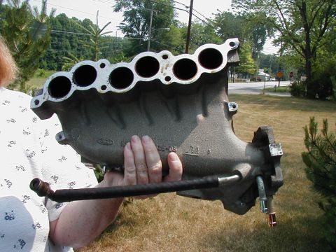 1997 Ford Taurus - A person holds up a Ford intake manifold, showing the six intake ports and some stamped lettering.