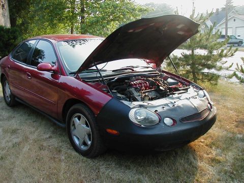 1997 Ford Taurus - A red sedan sits on grass with its hood open, revealing the engine compartment.