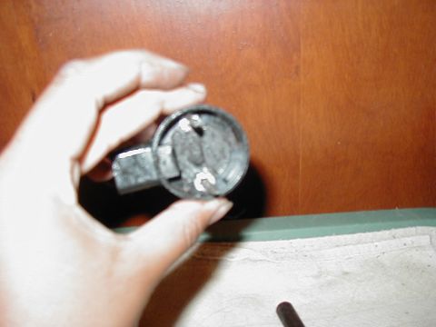 1997 Ford Taurus - A hand holds a metal automotive part, likely an electrical component, against a wooden background.