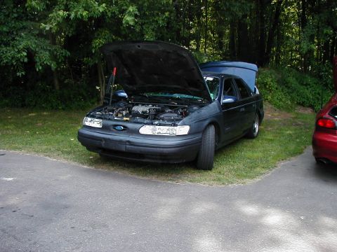 1997 Ford Taurus - A dark blue sedan sits with its hood and trunk open, parked on a grassy area next to a red vehicle.