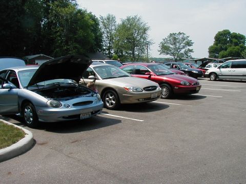 1997 Ford Taurus - A silver 1997 Ford Taurus is parked with its hood open, alongside other vehicles in a parking lot.