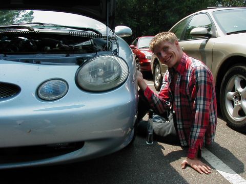 1997 Ford Taurus - Man works on the engine of a 1997 Ford Taurus, with other vehicles parked nearby.