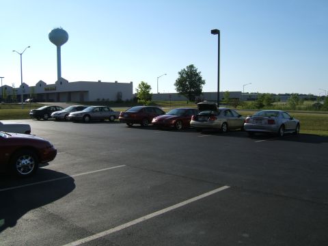 1998 Ford Taurus - A collection of cars are parked in a lot with a water tower in the background on a sunny day.