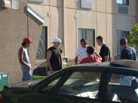 1998 Ford Taurus - Several men gather outside a motel building, with a car partially visible in the foreground.
