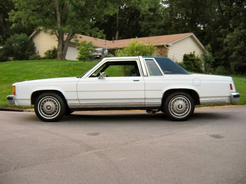 1985 Ford Crown Victoria LTD - Side profile of a white 1985 Ford Crown Victoria LTD two-door sedan parked on a residential street.