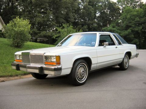 1985 Ford Crown Victoria LTD - A white 1985 Ford LTD Crown Victoria is parked on a residential street with trees in the background.