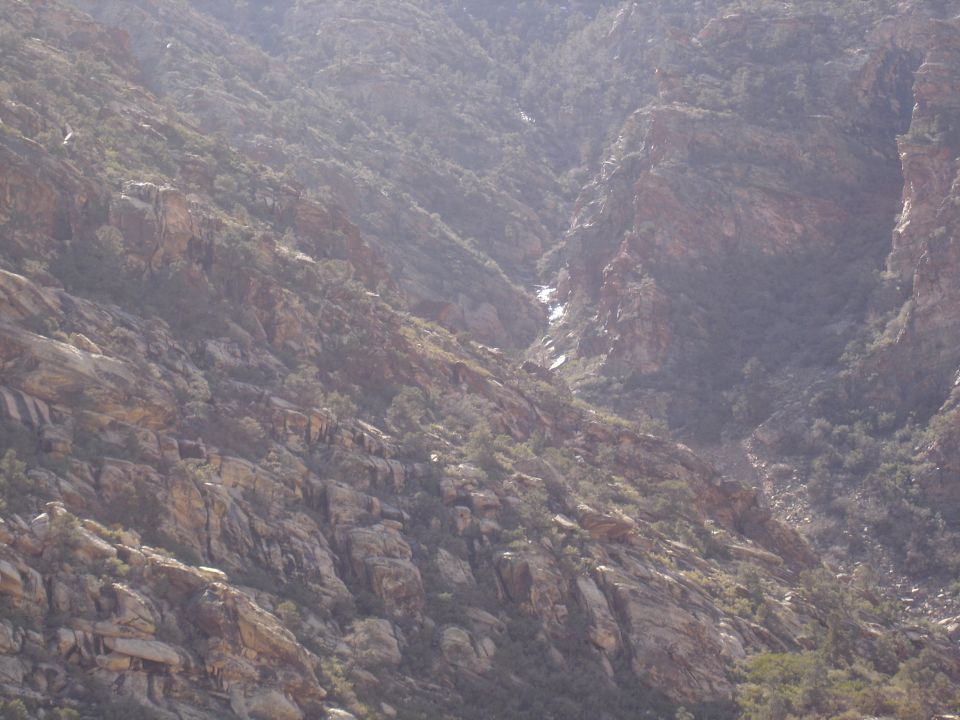 Hazy view of a steep rocky canyon with tan outcrops and scrub brush