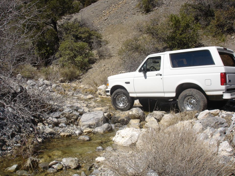 White Ford Bronco with hardtop on rocks beside a creek, side view