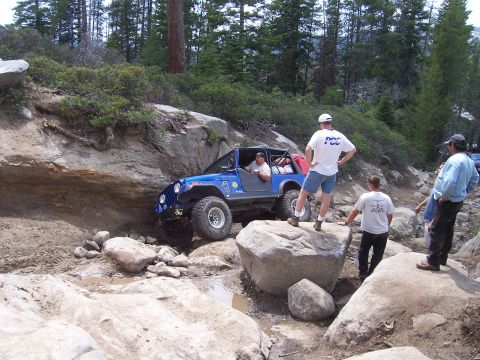 1998 Ford Ranger - A blue Jeep Wrangler tackles a challenging rocky terrain during an off-road excursion, with spectators observing the action.