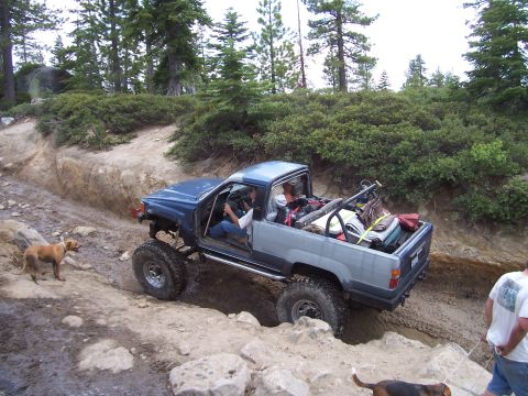 1998 Ford Ranger - Pickup truck off-roading on a rocky, muddy trail with trees and bushes in the background.