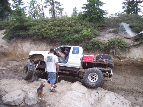 1998 Ford Ranger - A white pickup truck is being driven off-road by two men while a dog watches from the side.