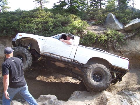 1998 Ford Ranger - This modified pickup truck is attempting a difficult off-road obstacle with a person watching.