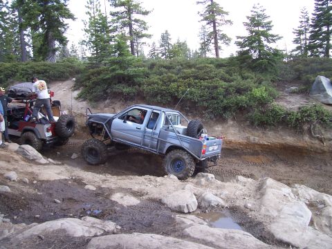 1998 Ford Ranger - Two modified off-road vehicles tackle a challenging rocky trail in a wooded area.
