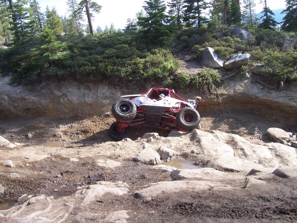 White off-road buggy with red roll cage climbing rocky terrain