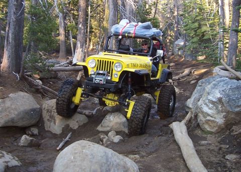 1998 Ford Ranger - Modified Jeep Wrangler tackling a challenging off-road course in a wooded area.