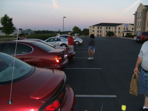 1998 Ford Taurus - Several cars are parked in a lot as people gather in the evening light.