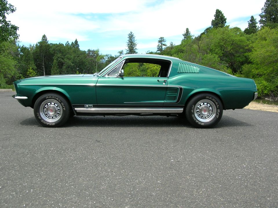 Dark green 1967 Ford Mustang fastback in side profile view on asphalt