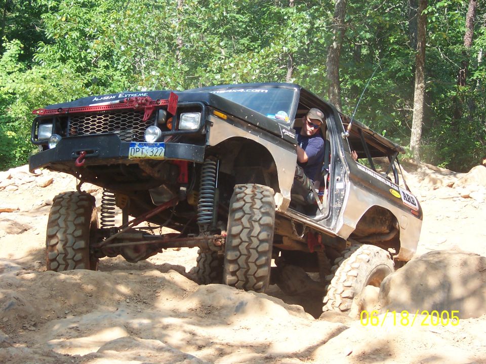 Modified Ford Bronco off-roading on a rocky trail. Driver is visible
