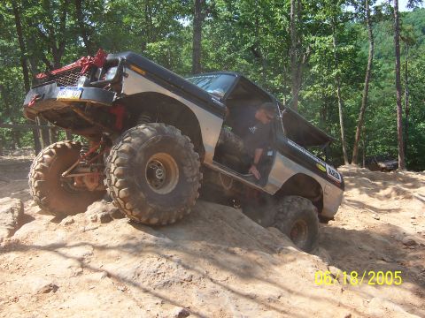 1978 Ford Bronco - This heavily modified SUV is tackling a challenging off-road trail, with its large tires gripping the loose dirt.