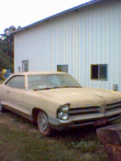 1994 Ford Bronco - This tan sedan, likely from 1965, is parked in front of a white building.