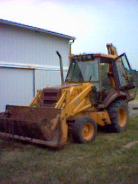 1994 Ford Bronco - Yellow backhoe loader with front loader parked outdoors next to a building.