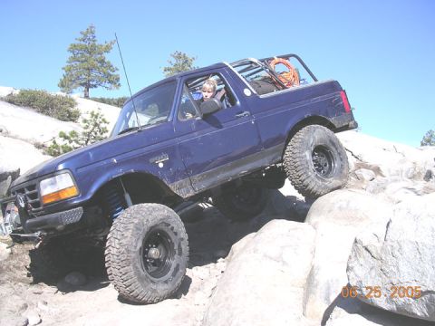1994 Ford Bronco - A blue 1994 Ford Bronco navigates a rocky trail on a sunny day.
