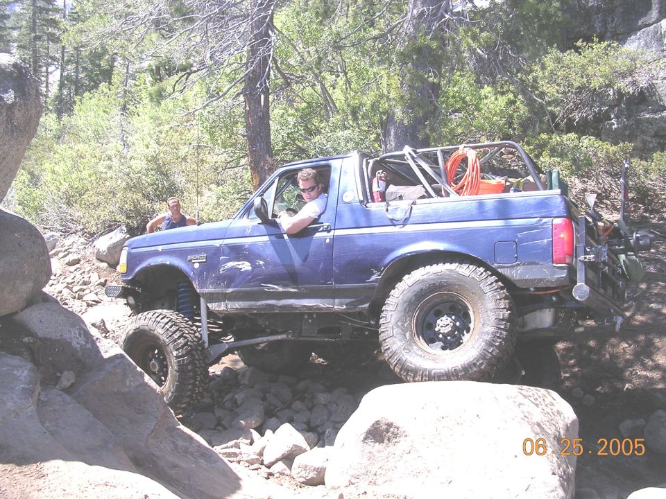 Blue 1994 Ford Bronco with roll cage and off-road tires navigating a rocky trail