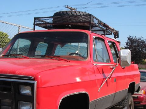1986 Ford Bronco - This red truck features a roof rack with a spare tire mounted on top, seen from a front quarter angle.