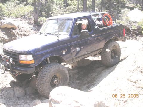 1994 Ford Bronco - A 1994 Ford Bronco is shown tackling a challenging off-road path with large rocks and dirt.