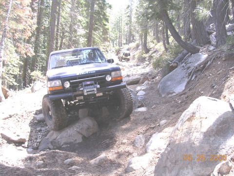 1994 Ford Bronco - A 1994 Ford Bronco navigates a challenging rocky trail in a forest setting, with another vehicle visible in the background.