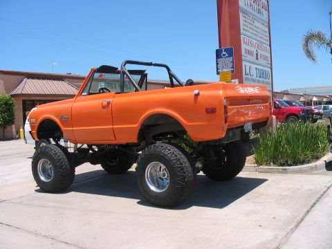 1986 Ford Bronco - This lifted orange SUV, likely a 1970s Chevrolet K5 Blazer, is shown from the side with its roll cage visible.
