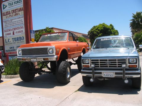 1986 Ford Bronco - Two lifted trucks are parked side-by-side on a sunny day.