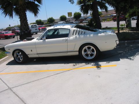 1986 Ford Bronco - Side view of a white 1965 coupe with black hood stripes and distinctive rear quarter window louvers.